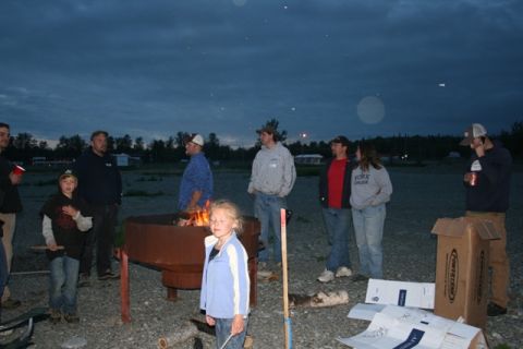 1990 Chevrolet Suburban - A group of people are gathered around a fire pit at dusk. A young girl in the foreground is looking down with her eyes closed.