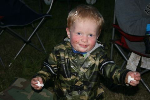 1990 Chevrolet Suburban - A young child wearing a camouflage jacket and with dirt and white substance on his face and hair smiles at the camera while holding two whi…