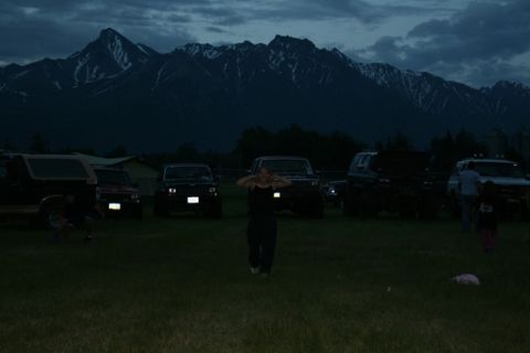 1990 Chevrolet Suburban - A group of off-road vehicles are parked in a grassy field at dusk, with a mountain range in the background. A person in the foreground appe…