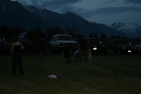 1990 Chevrolet Suburban - A group of people stand in a grassy field at dusk with several SUVs parked behind them, including a white Chevrolet Suburban.