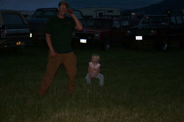 Man and child in grassy field with SUVs parked behind them at dusk.