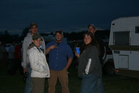 1990 Chevrolet Suburban - A group of five people are gathered in front of a white and brown travel trailer at dusk. The person on the far left is holding a black wat…