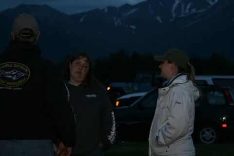 1990 Chevrolet Suburban - Three people stand in front of several parked vehicles with mountains in the background during twilight. The person on the left wears a bla…