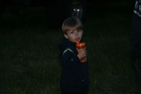 1990 Chevrolet Suburban - A young boy in a dark hoodie holds an orange sippy cup and looks towards the camera. He is standing in a grassy area at dusk.