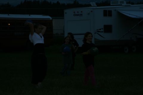 1990 Chevrolet Suburban - Four children are standing in a grassy field at dusk, holding balls. A trailer and a bus are visible in the background.