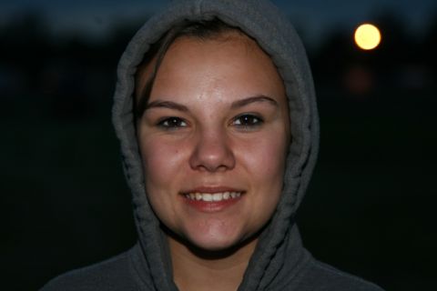1990 Chevrolet Suburban - A young woman wearing a gray hooded sweatshirt smiles at the camera. The background is dark with a blurred yellow light in the upper right…