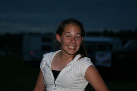 1990 Chevrolet Suburban - A young woman smiles at the camera at dusk. She is wearing a white zip-up hoodie over a black top.