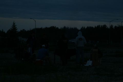 1990 Chevrolet Suburban - A group of people are gathered outdoors around a table at dusk. One person is wearing a hooded sweatshirt.