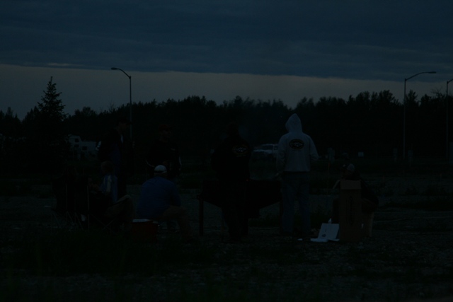 Group of people gathered around a table outdoors at dusk.