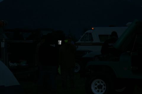1990 Chevrolet Suburban - In the dark, a group of people stand around several vehicles, including a white van with orange lights on top and a green Jeep with its hoo…