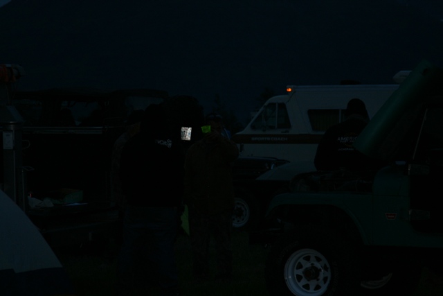 People gathered around vehicles at night, one Jeep has its hood open.