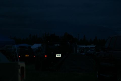 1990 Chevrolet Suburban - A dark, low-light image shows the rear of a dark-colored SUV parked among tents and other vehicles at dusk or night. The SUV has a license…