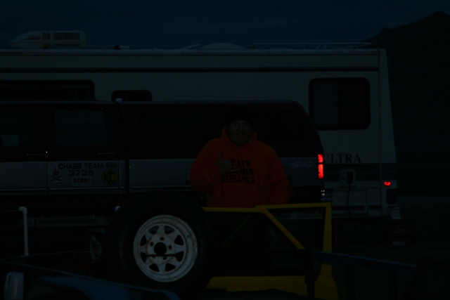 Person in orange hoodie giving thumbs up next to a trailer and van with RV in background.