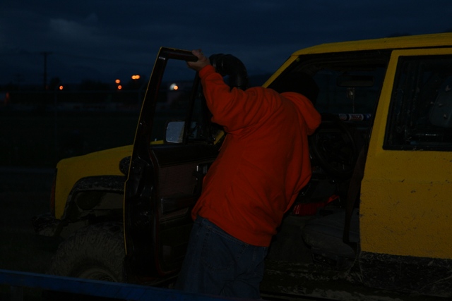 Person in orange hoodie entering yellow Jeep with open door at dusk.