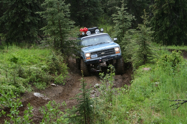 1990 Chevrolet Suburban off-roading on a muddy trail in a forest.