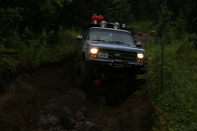 Lifted blue Chevrolet SUV driving on a muddy forest trail.