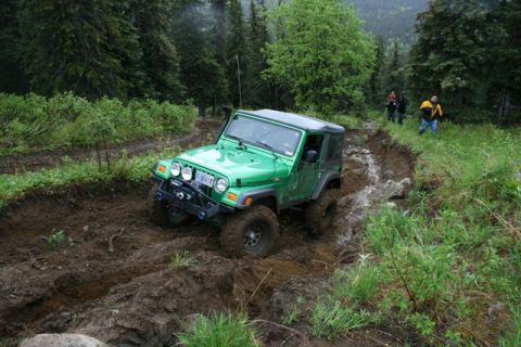1990 Chevrolet Suburban - A bright green Jeep Wrangler is navigating a deep, muddy rut on a wooded trail. Several people can be seen in the background further up the…