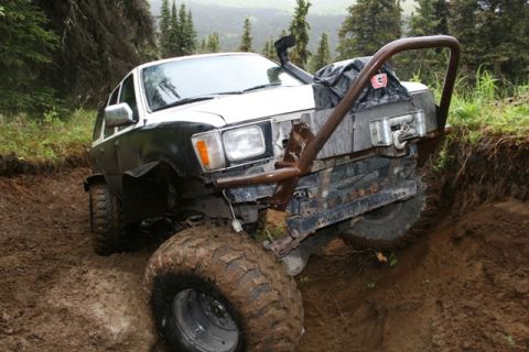 1990 Chevrolet Suburban - A modified white and black SUV is navigating a steep, muddy ditch on an off-road trail. The vehicle has large, aggressive tires and a custo…