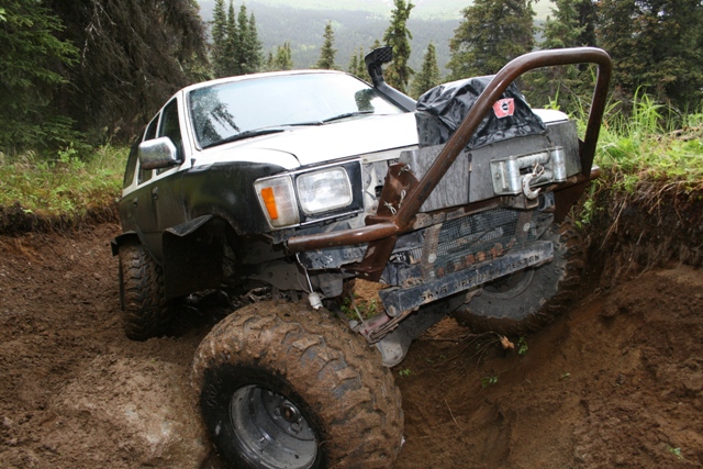 Modified white and black SUV with large tires and winch on a muddy off-road trail.