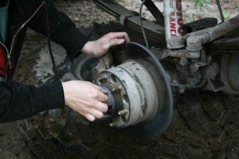 1990 Chevrolet Suburban - A person's hands are shown working on the brake rotor and hub assembly of a vehicle, which is resting on a muddy tire. The vehicle appears…