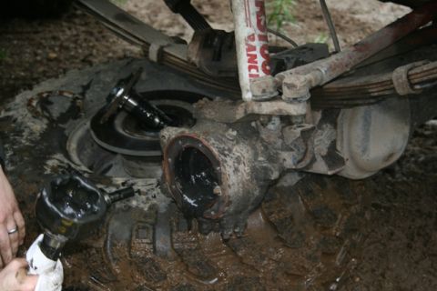 1990 Chevrolet Suburban - A close-up view of a vehicle's front differential housing and suspension components, covered in mud. A person's hands are visible, holding…