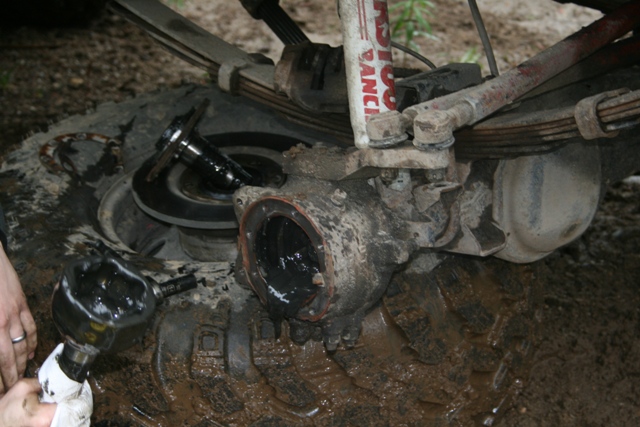 Mud-covered vehicle front differential and suspension components during repair.