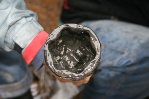 1990 Chevrolet Suburban - A close-up, top-down view of a person holding a container filled with dark, viscous mud or sludge. The container has a scalloped rim. The p…