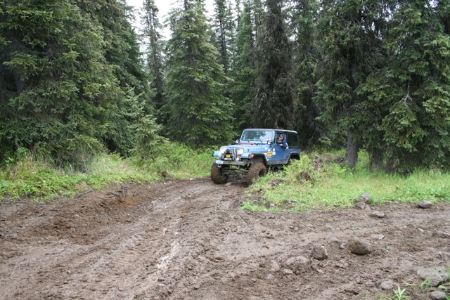 Blue Jeep Wrangler driving on a muddy forest trail