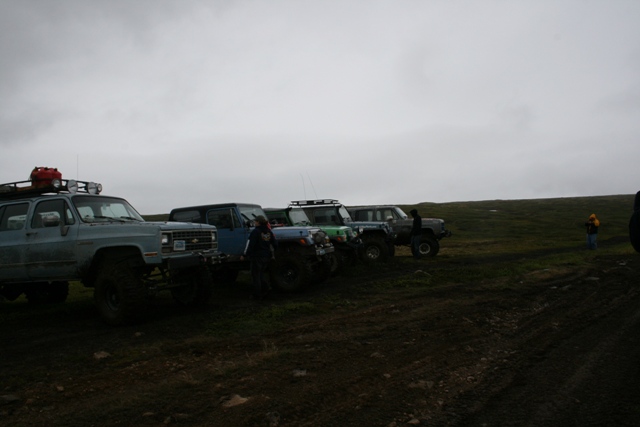 Light blue Chevrolet Suburban and other off-road vehicles on muddy terrain.