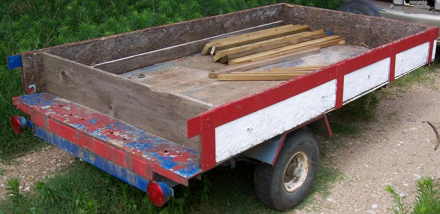 Side view of a weathered red and white utility trailer with lumber