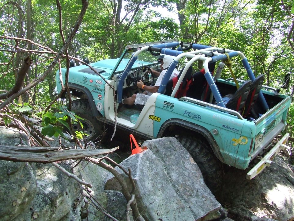 1967 Ford Bronco off-roading on a rocky, wooded trail.