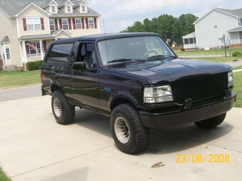 1996 Ford Bronco - A black 1996 Ford Bronco is parked on a concrete driveway in front of a suburban house. The vehicle is shown from a 3/4 front angle, highli…