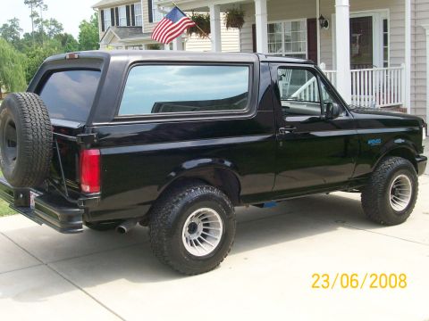 1996 Ford Bronco - The rear passenger side of a black 1996 Ford Bronco is shown parked on a concrete driveway in front of a house. The vehicle features a spar…