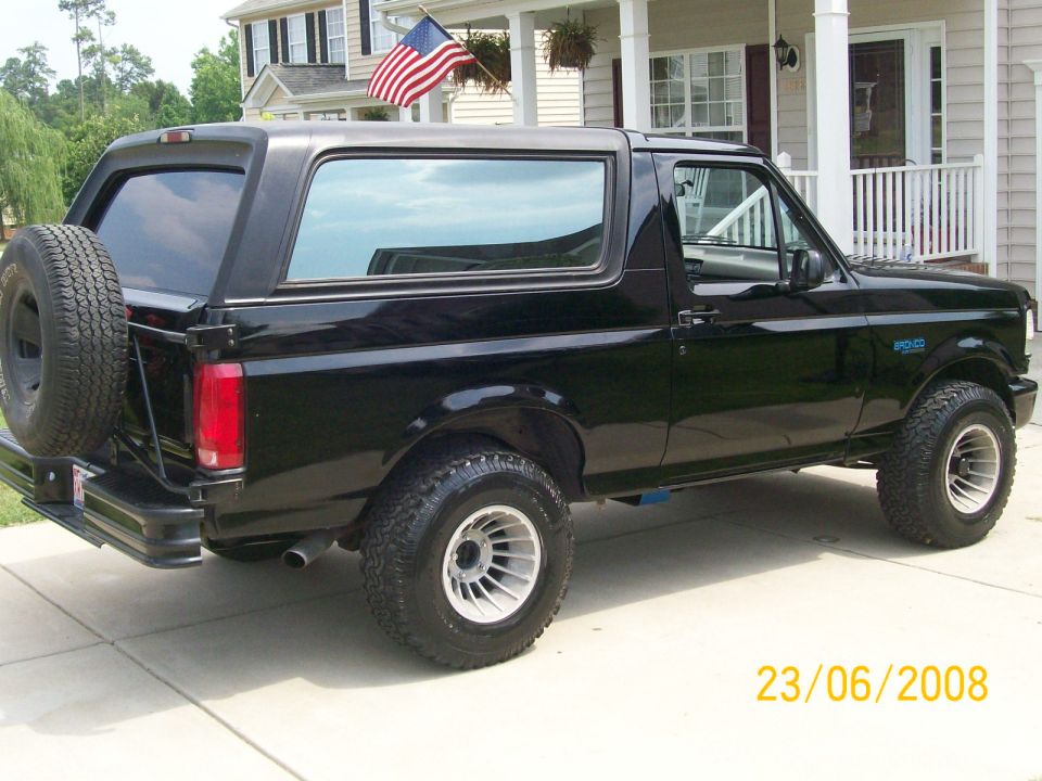 Black 1996 Ford Bronco rear passenger side view with spare tire and aftermarket wheels.