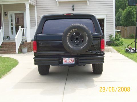 1996 Ford Bronco - The rear view of a black Ford Bronco parked in a driveway in front of a house. A spare tire is mounted on the rear exterior.