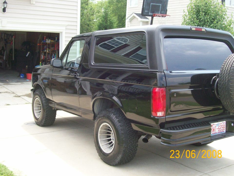 Black 1996 Ford Bronco parked in driveway, rear passenger side view, spare tire on back, license plate XWT-6658
