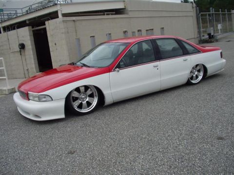 1998 Ford Crown Victoria - Side view of a lowered two-tone red and white Chevrolet Caprice sedan in front of a building.