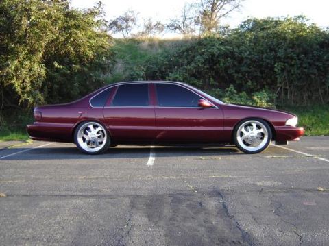 1998 Ford Crown Victoria - Side profile of a maroon Chevrolet Impala SS sedan on chrome wheels in front of shrubbery.