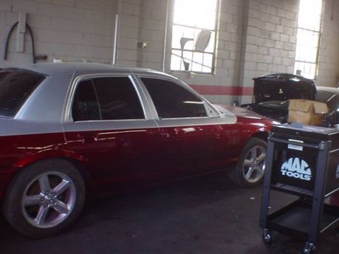 1998 Ford Crown Victoria - Side view of a two-tone red and silver sedan parked inside a repair garage with a Mac tool cart.