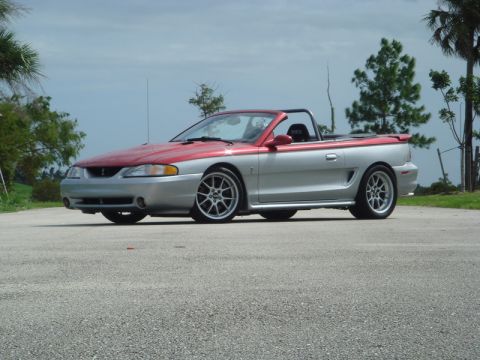 1998 Ford Crown Victoria - Front three-quarter view of a two-tone silver and red Ford Mustang convertible parked outdoors.
