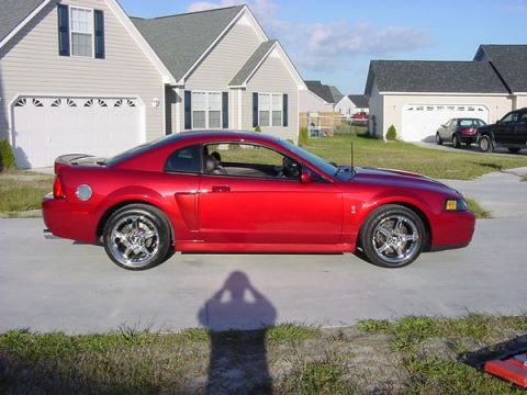 1998 Ford Crown Victoria - Side profile of a red Ford Mustang Cobra on chrome wheels parked in a residential driveway.