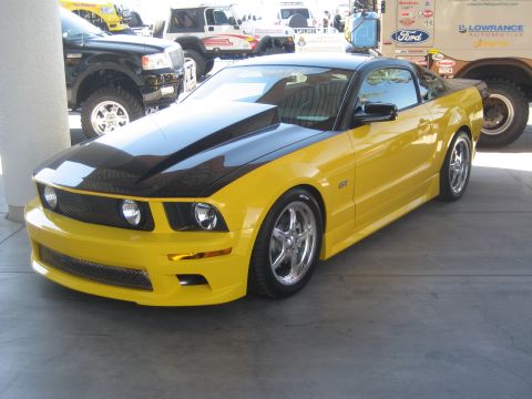 1998 Ford Crown Victoria - Front three-quarter view of a yellow Ford Mustang GT with black hood at an outdoor car event.