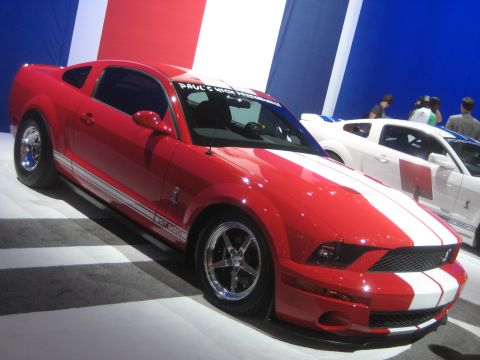 1998 Ford Crown Victoria - Front three-quarter view of a red Ford Shelby GT500 Mustang with white stripes at an auto show.