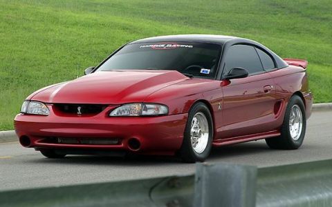 1998 Ford Crown Victoria - Photograph of a red Ford Mustang SVT Cobra coupe parked outdoors near a guardrail.