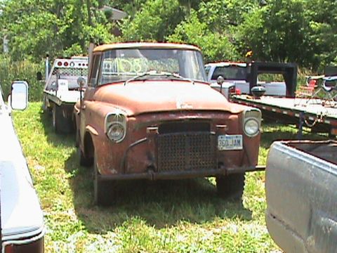 1987 Ford Bronco - A rusty, orange vintage pickup truck is parked on grassy ground, towing a flatbed trailer. The truck has a visible license plate that reads…