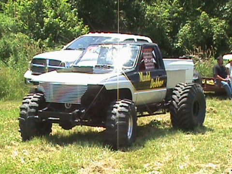 1987 Ford Bronco - A heavily modified pickup truck with oversized tires and a lifted suspension is parked on a grassy field. The truck has a custom grille, a…