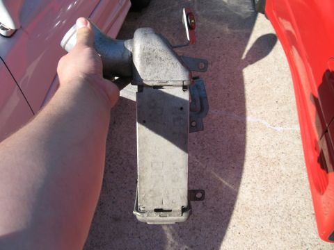 1991 Mitsubishi 3000GT - A hand holds a metal intercooler part, with the side of a red car visible in the background.