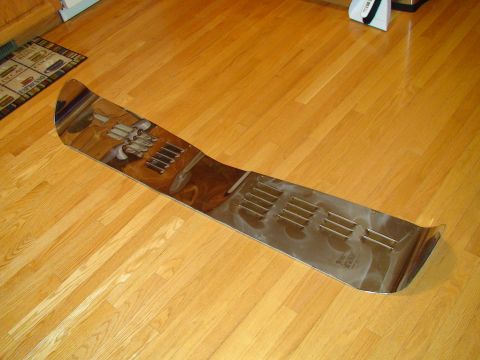 1979 Ford Bronco - A shiny chrome trim piece with multiple vent slots lies on a polished wooden floor.