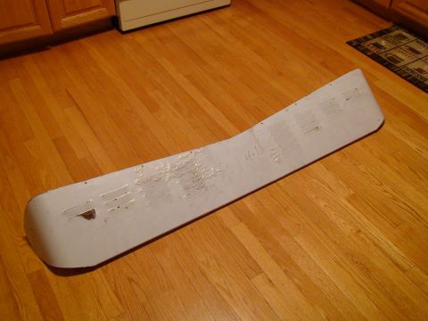 1979 Ford Bronco - A white car part, possibly a spoiler or trim piece, lies on a wooden floor with visible tape residue and handwritten notes.