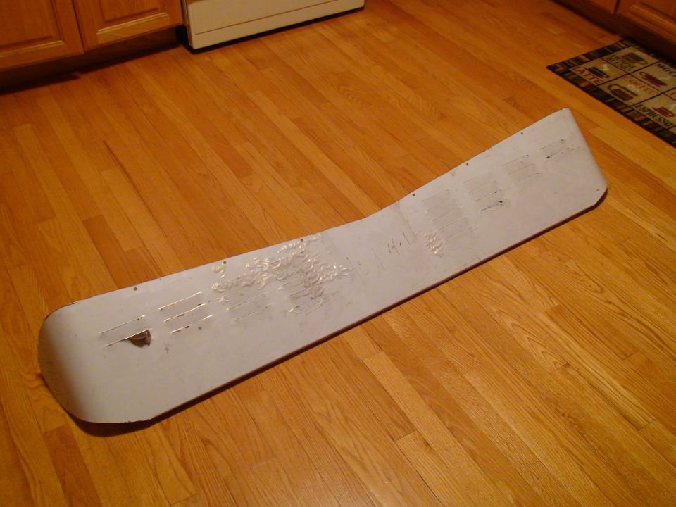 White car part with handwritten markings and tape residue on a wooden floor